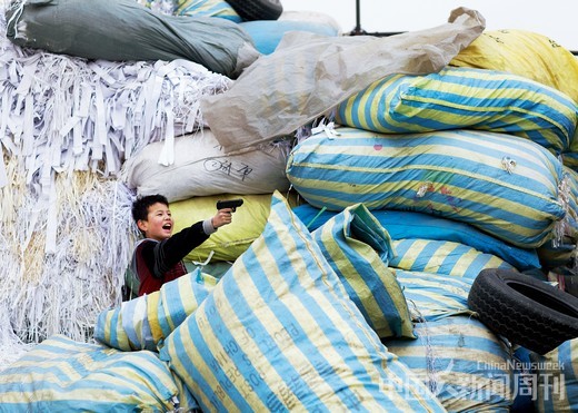 3月3日，北京昌平区，在废品回收集散地的废纸堆中玩枪的孩子。摄影/ 本刊记者 甄宏戈