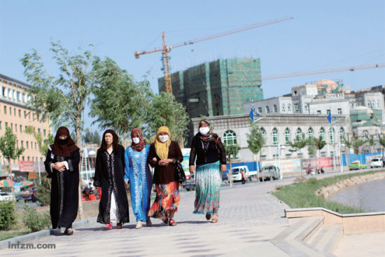 传统服饰女子背后是一片正在建设的楼房，喀什正在成为一个繁忙的工地。 (南方周末记者 麦圈/图)