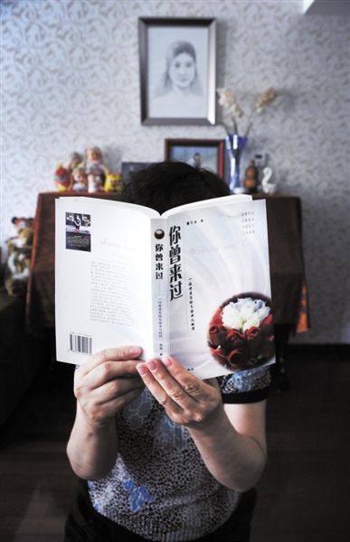 一名失独母亲，举着她写给女儿的书《你曾来过》，背后是女儿的钢琴和画像。