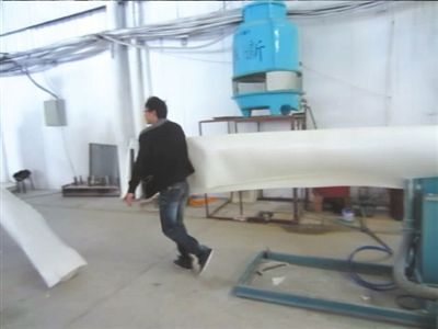 不穿工作服的工人徒手拉动用于生产发泡餐具的拉片。 