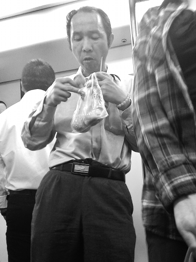 　　在轻轨车厢里，一名男子靠着立柱吃煎包。记者李少文 摄