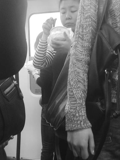 　　两名女子站在轻轨车厢里过早。 记者李少文 摄