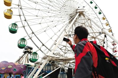 昨日，石景山游乐园，一游客在给乘坐摩天轮的妻儿拍视频。这座29岁的摩天轮将于月底“退役”。新京报记者 浦峰 摄