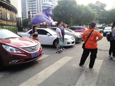 5月27日，朝外南街悠唐广场旁，一女停车管理员指挥一辆轿车停在斑马线上后继续招揽其他车辆。