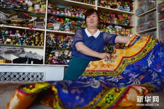 7月30日，在肃南裕固族自治县一家民族手工艺品店里，一位工人展示手工制作的裕固族传统服饰。 