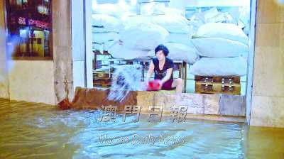 商户防水闸难挡潮水，唯有不停铲水泼门外。来源：《澳门日报》