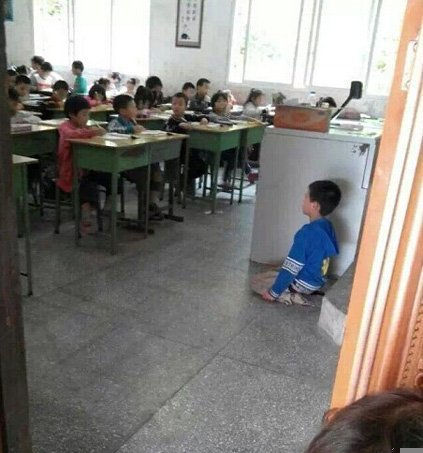 男孩面朝同学跪在讲台旁。