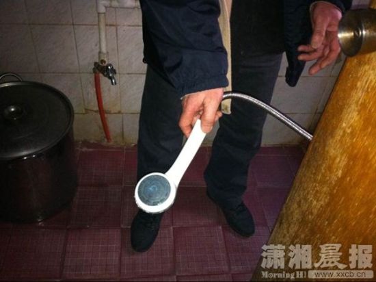 死者的父亲拿着热水器水龙头，介绍当日的情况。图/潇湘晨报记者陈正