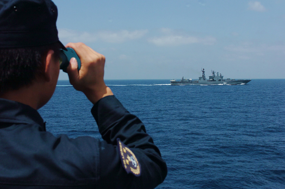 一名中国海军战士正在通过望远镜观察"特里布茨海军上将"舰的旗语