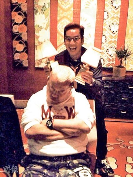 谭咏麟拿着两盏灯在好友曾志开后面作弄他。