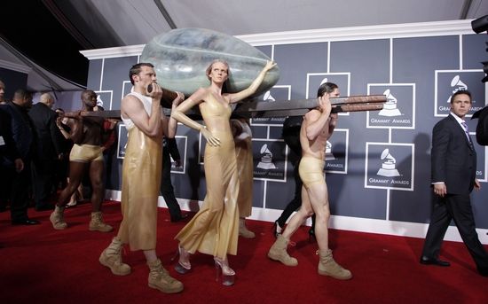 Lady Gaga不改搞怪本色，蜷缩在一个蛋形容器里，由身着金衣的随从抬着走过红地毯。