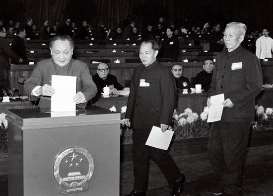 第五届全国人民代表大会第五次会议。1982年12月4日在人民大会堂举行全体会议。图为人大代表邓小平、胡耀邦、王震等投票表决宪法。图/新华