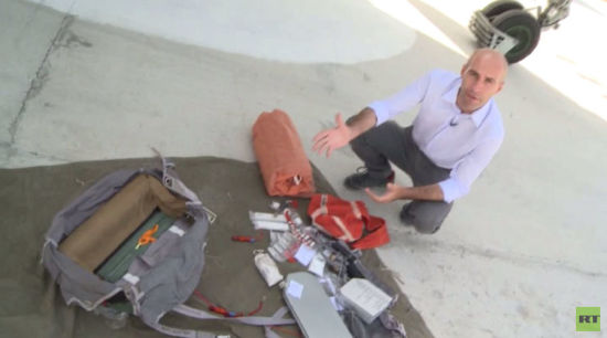 图中橙色大包为自充气式浮阀，在记者身前颜色较为鲜艳的橙色小包为自充气式无线电信标，图中下方灰色扁平容器为饮用水 